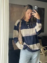 Sweater de hilo de algodón a rayas horizontales rosas y grises, con cuello polo, botones de guampa y bordado de Sierra Mora a tono.