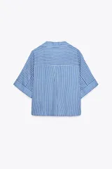 Camisa cropped de viscosa y lino a rayas verticales azules y blancas. Tiene cuello solapa, escote pico, manga corta con vuelta y bolsillos de plastrón.