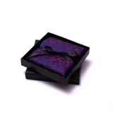 Pañuelo de bolsillo para traje o saco, color morado con estampado floral en azul. Viene presentado en una caja negra con un lazo de cinta de satén negro atado en forma de moño.
