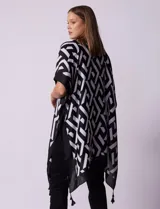 Kimono tejido con estampado geométrico en blanco y negro, ruedo con borlas y composición 100% poliéster.