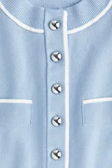 Saco corto celeste en tejido de punto con ribetes blancos en cuello, mangas, bolsillos y ruedo. Tiene cuello redondo, botones metálicos al frente y bolsillos superiores decorativos.
