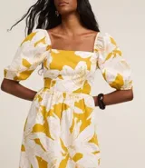 Vestido midi de tricolina con estampado floral en tonos amarillo y blanco. Tiene escote cuadrado, mangas abullonadas cortas, lastex en la espalda y recorte fruncido en la cintura.