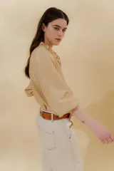 Blusa color beige con cuello mao con volantes, manga larga con puño elástico y cierre frontal con botones ocultos.