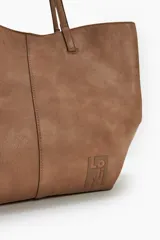 Cartera tote negra con doble asa de hombro y dije metálico circular con el nombre de la marca.