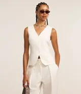 Chaleco de vestir color blanco hueso, con escote en V, cierre frontal con botones y espalda abierta. Corte sastrero.