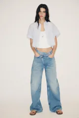 Camisa blanca corta con rayas verticales celestes, cuello solapa y mangas cortas con dobladillo. Tiene un bolsillo de parche en el pecho y cierre frontal con botones ocultos.