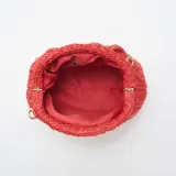 Bolso de mano tipo clutch, color rojo, confeccionado en rafia trenzada. Tiene forma rectangular con pliegues en la parte superior y cierre con broche imantado. Incluye una cadena dorada para usar como bandolera.