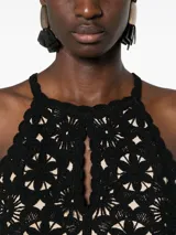 Top corto negro tejido a crochet con estampado floral, bordes festoneados y abertura en forma de lágrima.