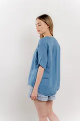 Camisa azul de lino con escote en V abotonado, bolsillo frontal y mangas 3/4 con trabilla.