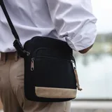 Morral bandolera negro de tela tafeta con detalles en símil cuero color beige. Tiene correa de galón regulable, cierre superior, dos bolsillos frontales con cierre y bolsillos internos.