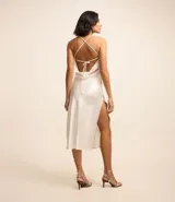 Vestido midi color blanco hueso de satén, con breteles finos, escote drapeado y lazo en la espalda. Presenta una abertura lateral en la falda.