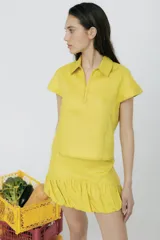 Blusa amarilla de lino con cuello polo, mangas cortas y cierre frontal con cremallera.