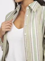 Camisa de manga larga a rayas verdes, marrones y blancas, confeccionada en lino y algodón. Tiene cuello clásico, cierre frontal con botones y corte holgado.