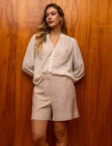 Blusa color crema de gasa bordada, con escote en V, abertura central con botones y mangas largas con puño.