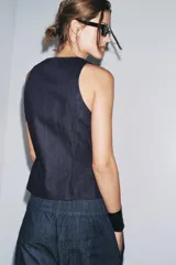 Top de denim color blanco, de cuello redondo y sin mangas. Cierre frontal con cremallera metálica.