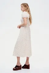 Vestido largo de algodón color crudo con estampado de pequeñas flores rosas, escote cuadrado, mangas cortas abullonadas con elástico y cuerpo fruncido.