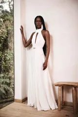 Vestido largo blanco de raso con cuello halter, abertura en el busto, pliegues, falda superpuesta y cremallera invisible en la espalda.
