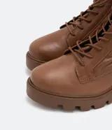 Bota de cuero color marrón con cordones, caña media con detalle de elástico en la parte trasera, taco bloque medio y suela track.
