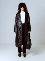 Trench largo de cuero negro con doble botonadura, solapas con muescas y costuras decorativas.