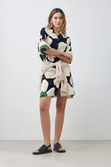 Vestido corto tipo túnica con cuello camisero, manga corta y estampado de margaritas en tonos blanco, verde y azul marino.