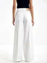 Pantalón blanco de lyocell, de corte acampanado con dos pliegues en la parte delantera de cada pierna. Tiene botón y cierre, además de dos bolsillos en la parte delantera y dos en la trasera.