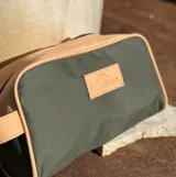 Neceser de lona verde con detalles en cuero color beige y etiqueta con logo de la marca Sierra Mora.