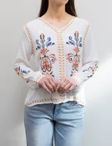 Blusa blanca de rayón con escote en V y mangas largas. Presenta bordados florales en tonos naranja, azul y negro en la parte delantera y en las mangas.