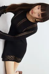 Vestido mini negro de manga larga en tejido de punto suave con escote redondo y falda con leve vuelo. Presenta secciones caladas en mangas, delantero y espalda, y secciones en punto pointelle en puños y bajo.