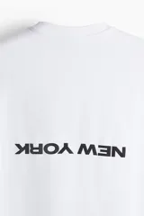 Remera blanca de corte holgado con cuello redondo y estampado pequeño con la frase "New York" en el pecho.