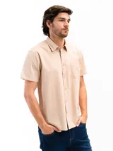 Camisa de manga corta color beige, confeccionada en 100% algodón, con cuello clásico, cierre frontal con botones y bolsillo en el pecho.