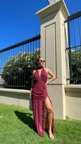 Vestido largo de microtul color rojo, con escote profundo en V y cuello halter. La falda presenta un diseño con frunces, transparencias y un tajo lateral pronunciado con detalle de volados.