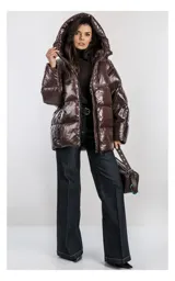 Campera oversize color blanco, confeccionada en nailon suave con un leve brillo. Cuenta con capucha, bolsillos laterales con cremallera, relleno natural y ajuste inferior con cordón. Presenta cierre frontal con cremallera de doble cursor y diseño acolchado.