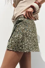 Falda pantalón verde militar con lentejuelas plateadas y negras, de tiro alto, con delantero cruzado y nudo.