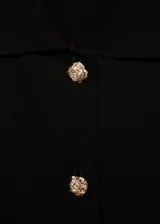 Chaleco negro sin mangas con cuello camisero, botones dorados con diseño de joya y corte entallado.