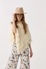 Poncho color crudo de lana merino, con flecos bordados a mano en el ruedo y escote en V.