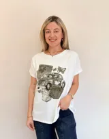 Remera blanca de algodón con estampado de un auto escarabajo rodeado de bolsillos de jean y mariposas.