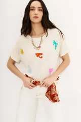 Remera color crudo de viscosa y poliéster, con moldería holgada, hombros caídos y mangas rebatidas. Presenta bordados de motivos egipcios en hilo de colores.