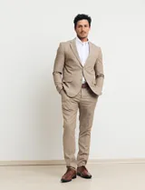 Traje de vestir color tostado, compuesto por saco con solapa de muesca, cierre de dos botones, bolsillos con solapa y pantalón de corte recto.