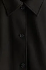 Campera corta negra de tejido de fieltro suave con cuello clásico y cierre frontal con botones. Modelo de corte holgado con hombros caídos y bolsillos insertados adelante.