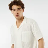 Camisa de manga corta color blanco hueso, de tejido calado con cuello solapa y bolsillo de parche en el pecho.