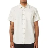 Camisa de manga corta color beige con estampado de flores pequeñas y bolsillo en el pecho. Cierre con botones marrones.