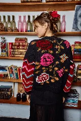 Sweater de lana tejido a mano color negro con bordado de flores rosas, naranjas y rojas. Tiene cuello redondo y mangas largas con puños ajustados.