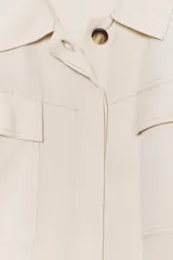 Vestido camisero largo color beige, de manga corta y cuello solapa. Tiene bolsillos de parche en el pecho, bolsillos laterales ocultos y cinturón de la misma tela.
