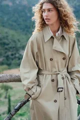 Gabardina midi color beige de algodón, con doble botonadura, cuello con solapas, cierre de corchete en la parte superior, solapa de tormenta en la espalda, bolsillos laterales con solapa, cinturón extraíble con hebilla rectangular, mangas raglán con trabilla ajustable en los puños y abertura trasera.