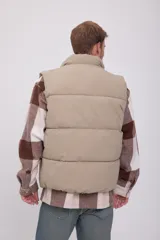 Chaleco acolchado sin mangas color beige, con cuello alto y cierre de cremallera.