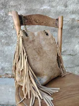 Bolso tipo bandolera color dorado con flecos y cadena metálica.