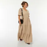Vestido largo color beige de tejido gofrado, con escote cruzado en V, mangas cortas abullonadas y falda amplia con corte en capas.