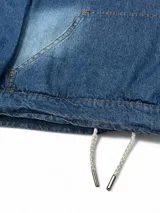 Canguro de jean azul con capucha, corte boxy y cordón ajustable en la cintura.