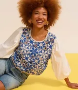 Blusa con cuerpo de tejido de ganchillo (crochet) bicolor azul y blanco con diseño floral, mangas largas abullonadas de tejido liso blanco y cuello redondo.