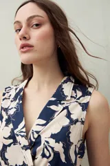 Vestido midi sin mangas con estampado floral y de hojas en tonos verde y marrón. Diseño cruzado tipo wrap con cuello sastrero y lazo ajustable en la cintura.